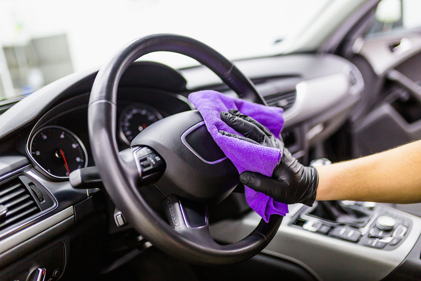 A Dapper Pros employee wiping down a steering wheel with a purple rag.